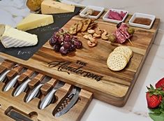 a cutting board with cheese, crackers and strawberries on it next to some fruit