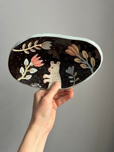 a hand holding up a decorative plate with animals on it's sides and leaves around the edges