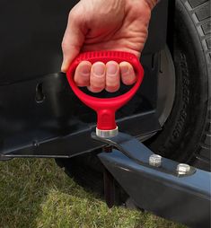 a hand holding a red wrench on the side of a car