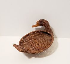 a wicker basket with a wooden duck head on the top and bottom, sitting on a white surface