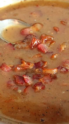 there is a bowl of soup with bacon in it and a spoon on the side