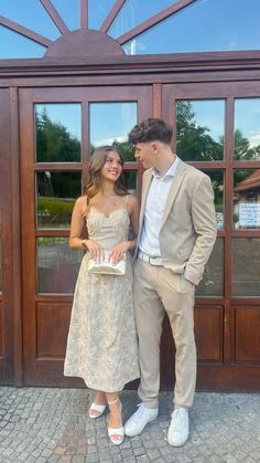 a man and woman standing next to each other in front of a wooden door with glass windows