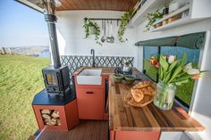 an outdoor kitchen with wood burning stove and wooden counter tops, surrounded by green grass