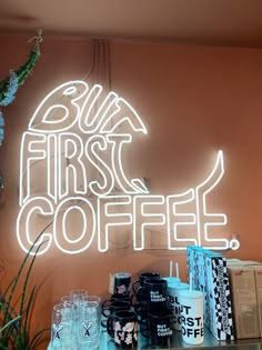 a neon sign that says, but first coffee on the wall behind it is filled with cups and mugs