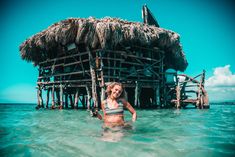 a woman standing in the water near a hut