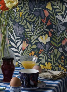 a table topped with cups and vases filled with flowers next to a wall paper