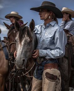 a woman in cowboy attire standing next to two horses