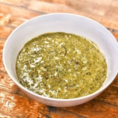 a white bowl filled with green sauce on top of a wooden table