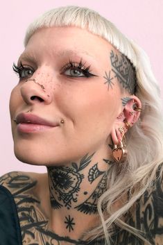 a woman with tattoos and piercings on her face is looking at the camera while wearing large gold hoop earrings