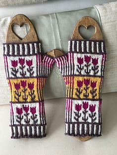 two pairs of knitted mittens hanging from hooks on a bed with pillows in the background