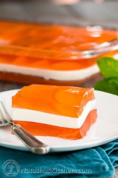 two pieces of cake on a white plate with silverware and green leaves in the background