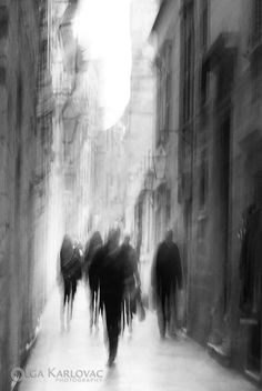 black and white photograph of people walking down the street in an old city with tall buildings