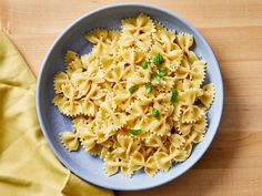 a blue bowl filled with pasta and parsley on top of a wooden table next to a yellow napkin