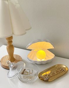 a white table topped with a lamp next to a glass bowl and tray on top of it