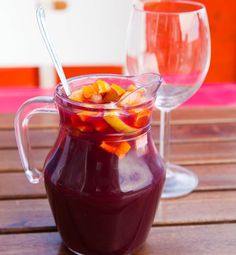 a glass jar filled with fruit sitting on top of a wooden table next to two wine glasses