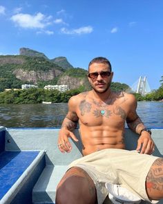 a shirtless man sitting in the back of a boat with tattoos on his chest