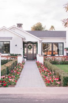 a white house with red flowers in the front yard and walkway leading up to it