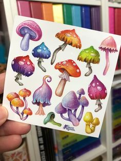 a person holding up a sticker with different colored mushrooms on it