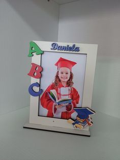 a photo frame with a child's graduation cap and gown holding a book in front of it