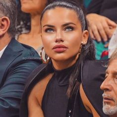 a woman sitting next to an older man in front of people at a tennis match