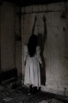 a woman with long hair standing in an old room holding her hand up to the ceiling