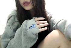 a woman with long brown hair wearing a gray sweater and blue zz logo on her arm