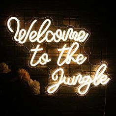 a neon sign that says welcome to the jungle in white letters on a brick wall