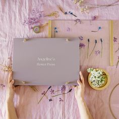 two hands are holding a box with flowers on the table next to it and other items