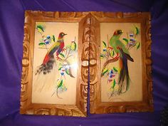 two framed pictures with birds on them sitting on a purple cloth covered tablecloth next to each other