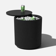 a black trash can with two cans in it and some ice on the table next to it