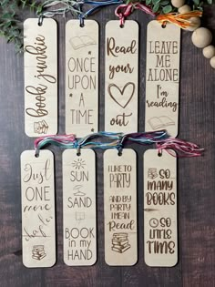 four wooden bookmarks with handwritten words on them hanging from a wood table next to christmas decorations