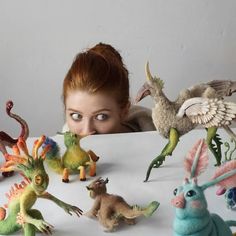 a woman looking over a table with many toy dinosaurs and birds in front of her