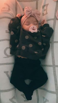 a baby is laying down on a bed wearing a polka dot shirt and black pants