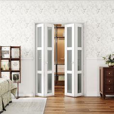 a bedroom with white walls and wooden floors, two doors open to reveal another room