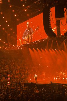 a man playing guitar on stage in front of an audience at a concert with bright lights