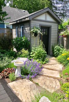 an outdoor garden with flowers and plants around the house, along with a birdbath