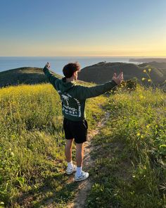 a man standing on top of a lush green hillside next to the ocean with his arms wide open