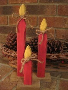 two red candles sitting on top of a table next to a basket filled with pine cones