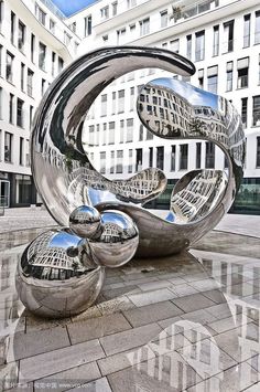 a large metal sculpture sitting in the middle of a street next to tall white buildings