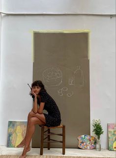 a woman sitting on top of a wooden chair next to a chalkboard drawing wall