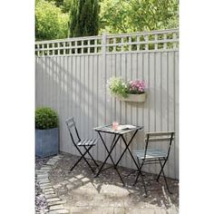 two chairs and a table in front of a fence with potted plants on it