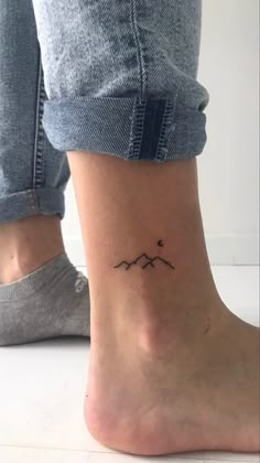 a woman's foot with a small mountain tattoo on the side of her ankle