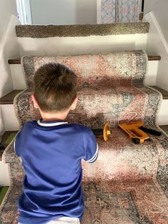 a young boy sitting on top of a carpeted stair case next to a rug