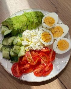 a white plate topped with sliced up tomatoes and avocado next to hard boiled eggs