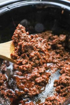 a wooden spoon full of ground beef in a crock pot with sauce on top