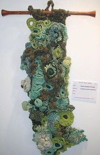 a crocheted piece hanging on a wall next to a wooden stick and sign