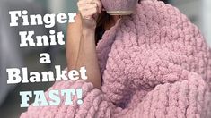 a woman wrapped in a pink blanket holding a coffee cup with the words finger knit a blanket fast