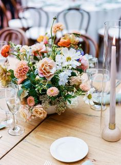 an arrangement of flowers in a vase on top of a table with plates and silverware