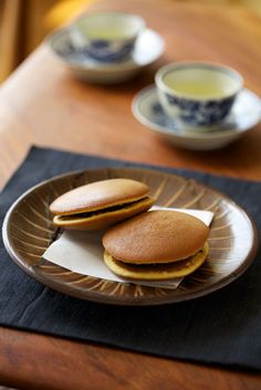 two biscuits on a plate with tea cups in the background