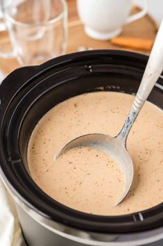 a spoon in a crock pot filled with creamy cream and brown sugar, on a wooden table